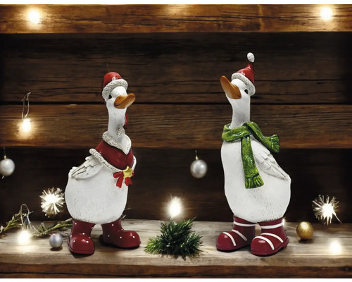 Zwei dekorative Gänsefiguren mit Weihnachtsmützen, Schals und Stiefeln auf einem Regal.