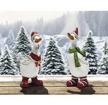 Zwei dekorative Gänsefiguren mit Weihnachtsmützen und Schals vor verschneiter Waldkulisse.