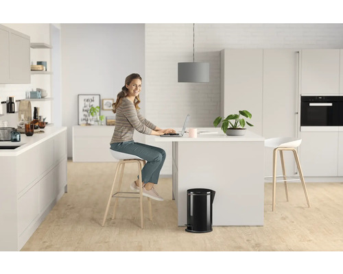 Femme travaillant sur un ordinateur portable dans une cuisine lumineuse avec îlot de cuisine et poubelle