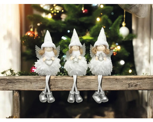 Drei dekorative Engel auf einem Sims vor einem Weihnachtsbaum