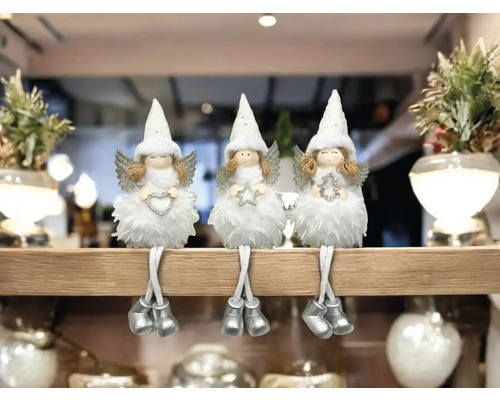 Drei weisse Weihnachtsengel-Figuren mit Zipfelmützen, Flügeln und silbernen Schuhen sitzen auf einem Regal.