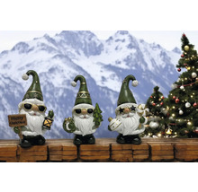Drei weihnachtliche Gartenzwerge mit Sonnenbrille vor verschneiter Bergkulisse und Tannenbaum