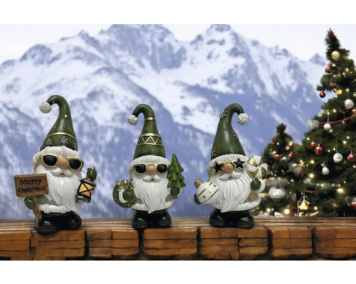 Drei weihnachtliche Gartenzwerge mit Sonnenbrille vor verschneiter Bergkulisse und Tannenbaum