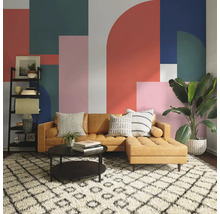 Salon avec canapé marron, table basse, étagère et plante d''intérieur devant un mur à motifs géométriques