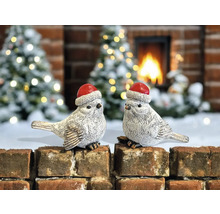 Deux oiseaux décoratifs avec des bonnets de Noël sur un mur de briques devant une cheminée et des sapins de Noël