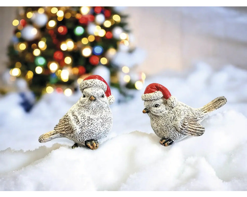 Zwei dekorative Vögel mit Weihnachtsmützen vor einem Weihnachtsbaum.
