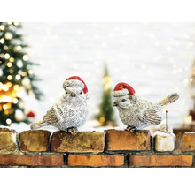 Deux oiseaux décoratifs avec des bonnets de Noël sont posés sur un mur en briques