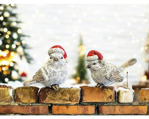 Zwei dekorative Vögel mit Weihnachtsmützen sitzen auf einer Ziegelmauer
