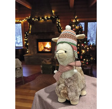 Dekoratives Lama mit Mütze und Schal vor Kamin und Weihnachtsbaum.