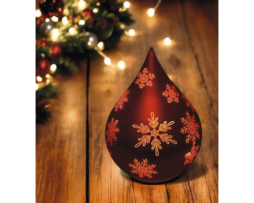 Dekorative Weihnachtslampe in Tropfenform mit Schneeflockenmuster auf einem Holztisch, festliche Beleuchtung im Hintergrund.