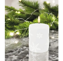 Bougie décorative à motif de flocons de neige devant des branches de sapin et des lumières.