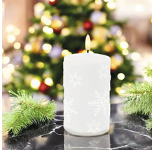 Bougie LED blanche décorative avec motif de flocon de neige devant un sapin de Noël