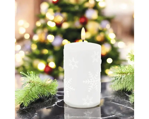 Bougie LED blanche décorative avec motif de flocon de neige devant un sapin de Noël
