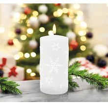 Bougie pilier décorative avec motif de flocons de neige devant un sapin de Noël et des cadeaux