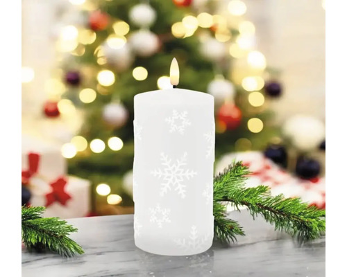 Bougie pilier décorative avec motif de flocons de neige devant un sapin de Noël et des cadeaux