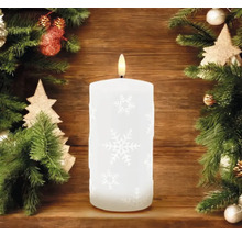 Bougie LED décorative avec motif de flocons de neige et lumière blanc chaud, entourée de branches de sapin et de décorations de Noël.