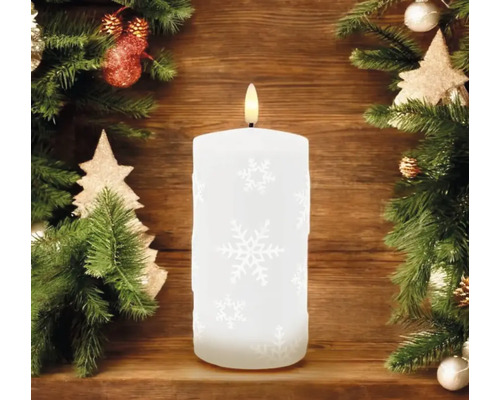 Bougie LED décorative avec motif de flocons de neige et lumière blanc chaud, entourée de branches de sapin et de décorations de Noël.