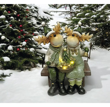 Des figurines décoratives d''élan sont assises sur un banc avec des arbres de Noël en arrière-plan.