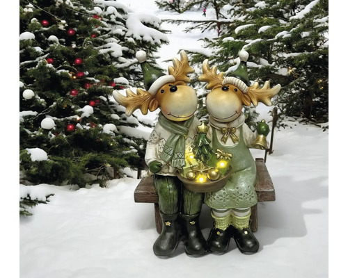 Des figurines décoratives d''élan sont assises sur un banc avec des arbres de Noël en arrière-plan.