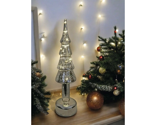 Dekorativer Weihnachtsbaum aus Glas mit Beleuchtung neben dekoriertem Tannenbaum