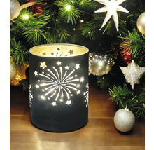 Dekorative Windlichtlaterne mit ausgeschnittenen Sternen und Feuerwerksmotiven vor einem geschmückten Weihnachtsbaum.