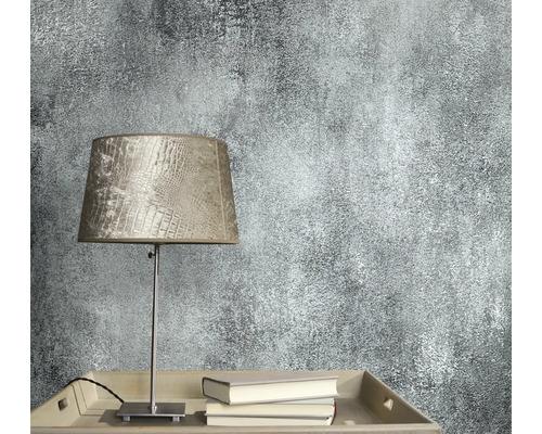 Nahaufnahme einer Wandtapete mit abstraktem Muster neben einer Lampe und Büchern.