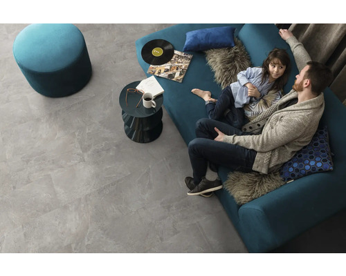 Wohnzimmer mit grauen Bodenfliesen, blauem Sofa, Hocker und Beistelltisch