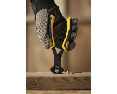 Eine Hand in Arbeitshandschuhen hält eine Kneifzange über einem Holzbrett, auf dem Nägel liegen.