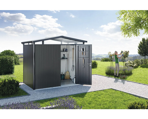 Abri de jardin avec porte ouverte dans un paysage de jardin avec pelouse et une femme taillant des roses.