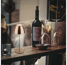 Dekorative Tischleuchte aus Metall neben einer Flasche Wein und Weingläsern auf einem Holztisch.