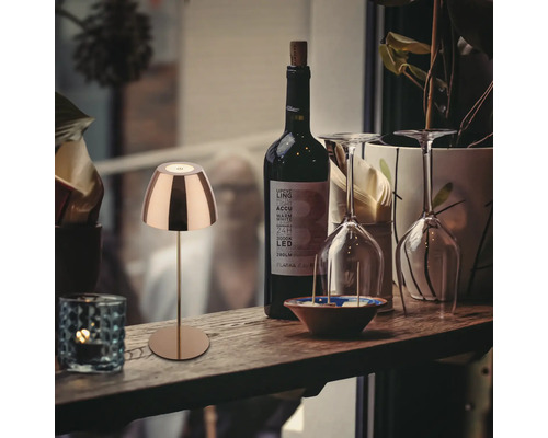 Dekorative Tischleuchte aus Metall neben einer Flasche Wein und Weingläsern auf einem Holztisch.