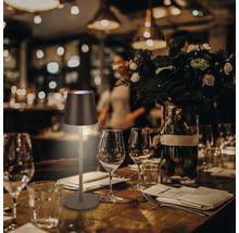 Tischszene mit einer LED-Tischleuchte auf einem gedeckten Holztisch mit Gläsern und Besteck