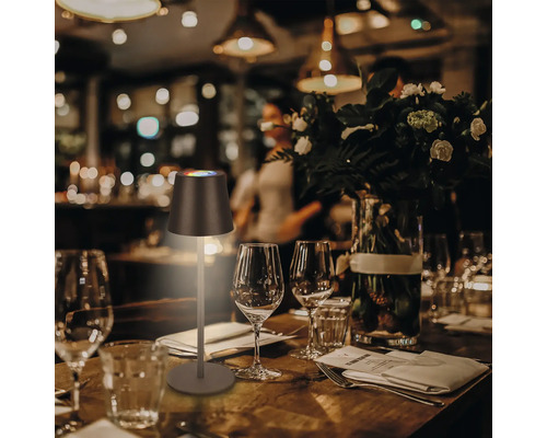 Tischszene mit einer LED-Tischleuchte auf einem gedeckten Holztisch mit Gläsern und Besteck