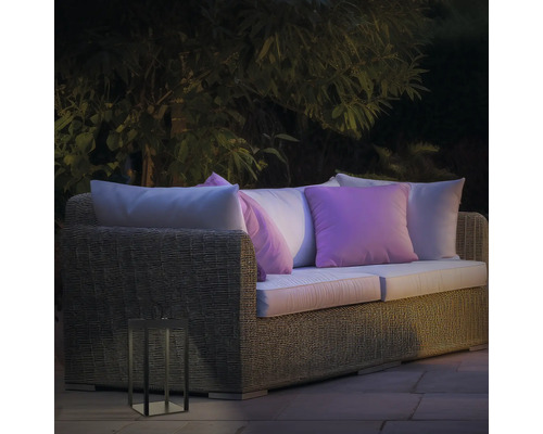 Gartenszene mit Rattan-Lounge-Sofa, Kissen und dekorativer Laterne für den Aussenbereich