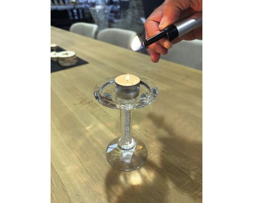 Eine Person zündet eine Kerze in einem Kristallkerzenständer mit einem Stabfeuerzeug an.