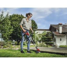 Frau benutzt einen Akku-Rasentrimmer im Garten.
