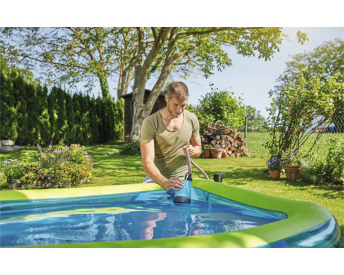 Mann benutzt eine Tauchpumpe, um Wasser aus einem Schwimmbecken im Garten abzupumpen.
