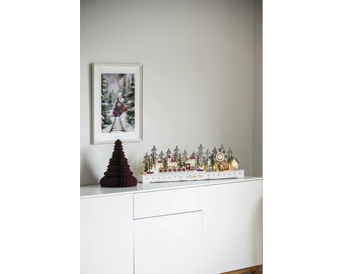 Dekorative Weihnachtsszene mit beleuchteter Winterlandschaft, Papierbaum und Zugbild auf einem weißen Schrank