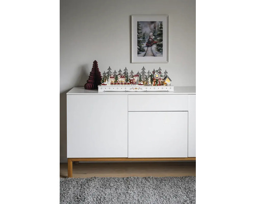 Dekorative Weihnachtslandschaft mit Häusern, Bäumen und Zug auf einem Sideboard
