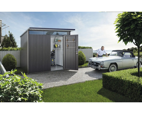 Abri de jardin en métal avec portes ouvertes, étagères, nettoyeur haute pression et un homme qui nettoie une voiture.