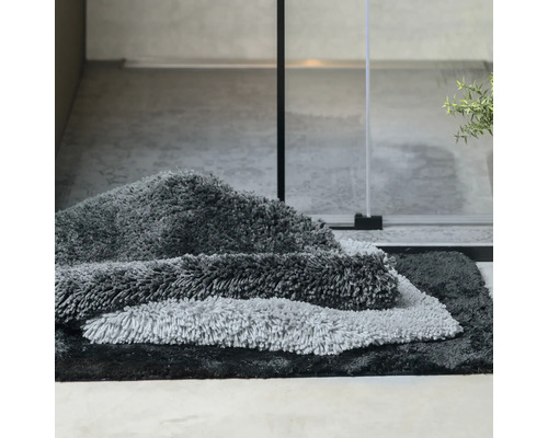 Mehrere Badteppiche in Grautönen gestapelt im Badezimmer.