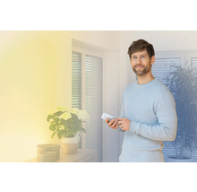 Mann bedient mit einer Fernbedienung ein Smart Home System in einem hellen Wohnraum.