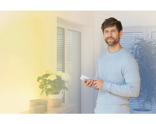 Mann bedient mit einer Fernbedienung ein Smart Home System in einem hellen Wohnraum.