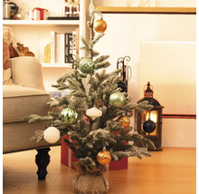 Petit sapin de Noël décoré sur le sol avec des cadeaux et des décorations en arrière-plan.