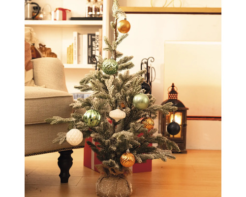 Petit sapin de Noël décoré sur le sol avec des cadeaux et des décorations en arrière-plan.