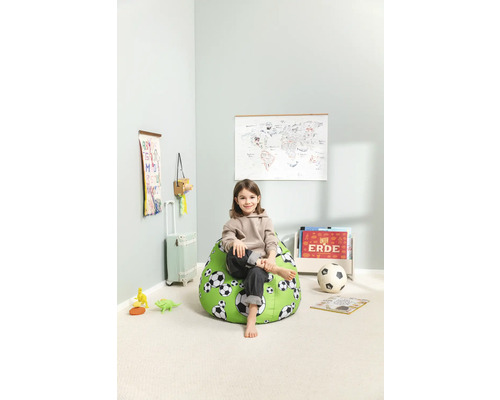 Ein Kind sitzt auf einem grünen Sitzsack mit Fußballmuster in einem hellen Zimmer.