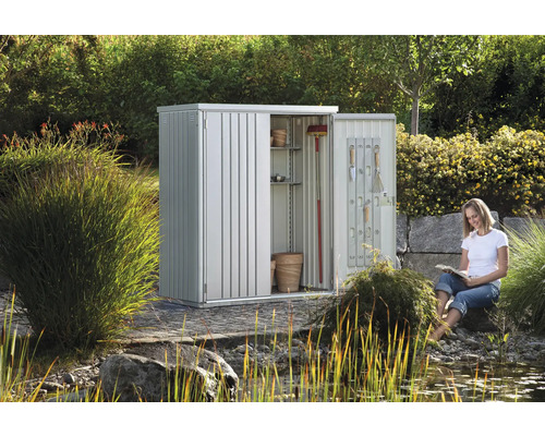 Gartenschrank aus Metall mit geöffneter Tür und lesender Frau im Garten