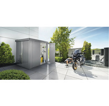 Szene im Garten mit Gerätehaus, in dem ein Hochdruckreiniger und Regale zu sehen sind. Ein Mann repariert ein Motorrad vor dem Gerätehaus.