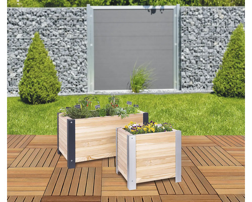 Zwei Pflanzkästen aus Holz mit Kräutern und Blumen auf einer Terrasse, im Hintergrund ein Garten mit Zaun.