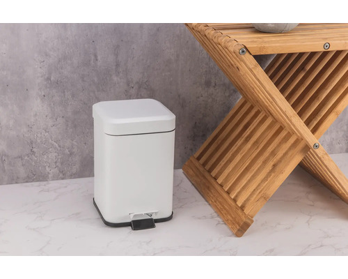 Poubelle à pédale blanche en métal à côté d''un tabouret en bois